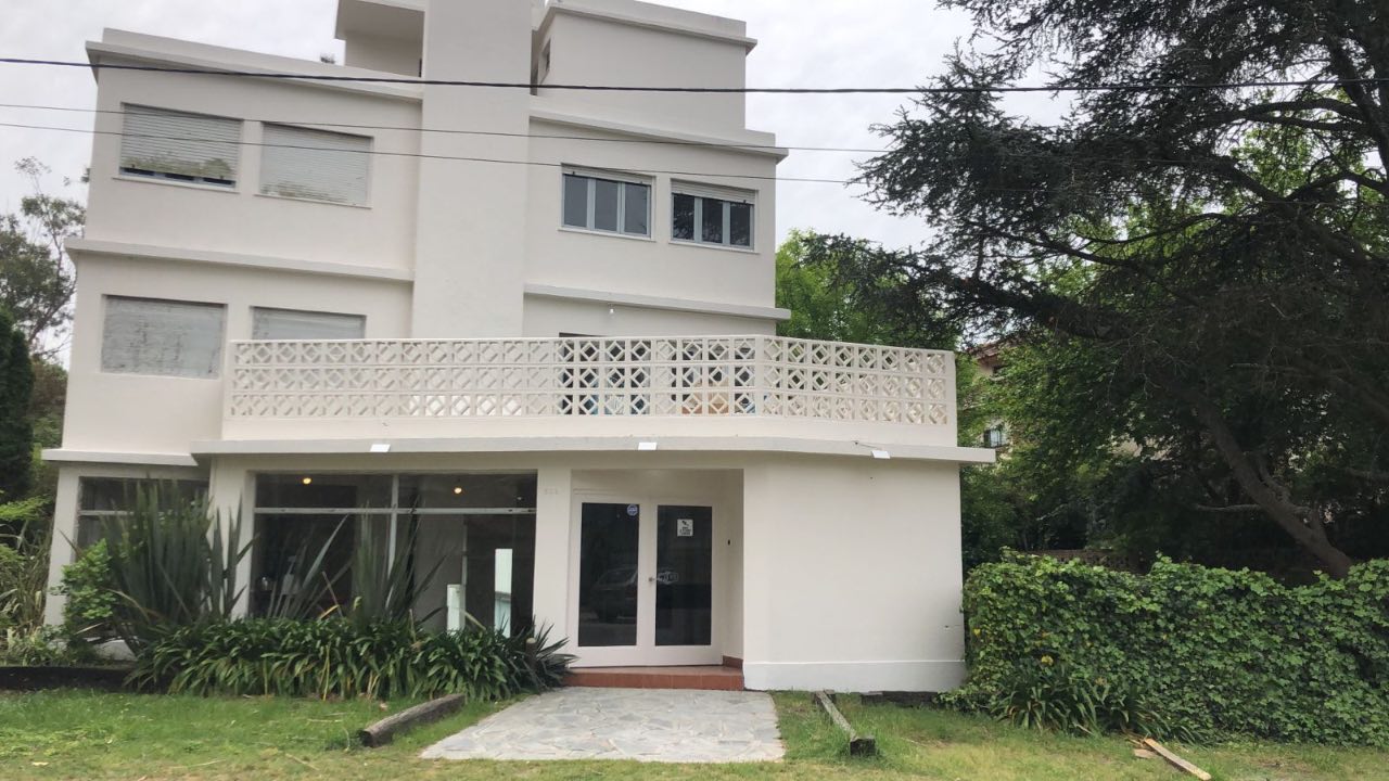 Fachada de Bunkker Pinamar - Edificio blanco con balcón y jardín