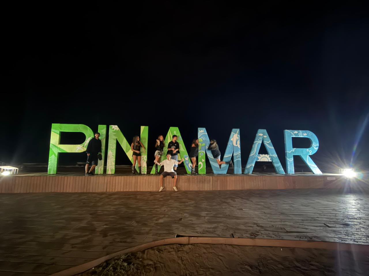 Grupo de huéspedes frente al cartel de Pinamar iluminado de noche